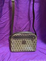 Full view of small cross body purse on purple cloth, showing beige and brown geometric pattern with brown leather strap and trim.