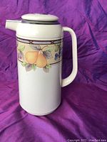 Side view of white ceramic carafe with retro fruit pattern on purple background