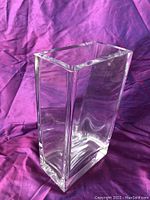 Large modern thick glass vase photographed on a purple fabric background showing its rectangular shape and clear glass material.