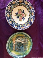 Top side of large hand-painted ceramic plate with floral and shell design, laid on purple fabric