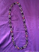Silver-plated necklace laid out over purple fabric background showing alternating flower links and colored beads.