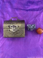 Mini brass treasure/jewelry box with two beads on purple fabric background