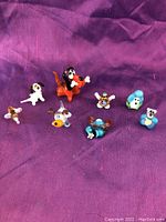 Top-down view of 8 miniature colorful glass animal figurines on a purple cloth background.