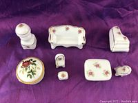 Miniature porcelain antique furniture pieces and round porcelain box displayed on purple fabric
