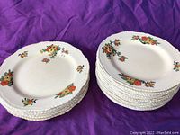 Stacks of white plates with hand-painted orange and yellow floral designs on a purple fabric background showing both dinner and appetizer plates.