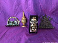 Photo showing four distinct Judaica items on a purple background: two oil menorahs, one with Hebrew and cityscape design, one with a crown motif; a silver-colored piece with a detailed relief; and a brass/bronze ornamental decorative piece.