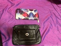 Floral patterned wallet and black leather clutch side by side on purple fabric background.