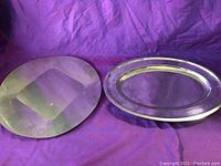 Two silver-colored stamped metal serving platters on a purple cloth. One oval with smooth rim, other irregular and textured.