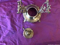 Top view of the antique food trivet with removable heat warmer on a purple cloth background. Shows central lid and ornate scroll handles.
