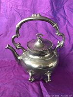 Front angle photo showing the teapot's detailed handle, lid with finial, rounded body, spout, and legs
