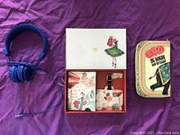Photo showing blue wired headphones next to a decorated box containing a matching wallet, passport case, and luggage tag.