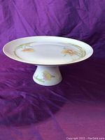 Pedestal cake tray with painted floral accents on stand and surface.