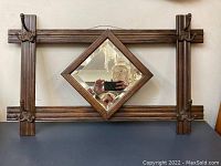 Front view of the entire antique coat rack showing wooden frame, diamond-shaped beveled mirror in the center, and four metal hooks on the corners.