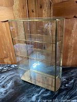 Full front and side view of the brass and glass display case on a black marble surface with wood panel background
