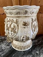 Front view of large vintage plaster pot displaying ornate acanthus leaf and scrollwork relief decoration and scalloped rim.
