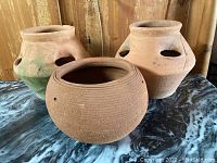 Three terra cotta pots displayed on marble surface with wooden background