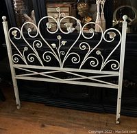 Full front view of white decorative metal twin headboard showing its overall height and width against black background and wooden floor.