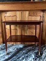 Front view of the wooden bar cart showing two shelves and four tapered legs with casters.