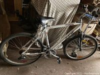 Side view of the full white CCM Nevada 26 FS Comfort bicycle showing wheels, frame, handlebars, and seat, on a dirt floor.