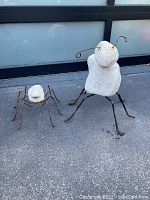 Two garden insect decor figures with stone bodies and iron legs and antennas, shown outside on pavement.