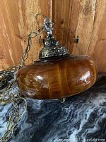 Close-up of amber glass globe with detailed metal fixture top and hanging chain for swag installation.