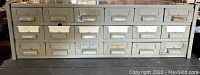 Front view of rectangular metal cabinet with 20 drawers arranged in two flush rows. Gray paint finish with metal handles and label holders on the drawers.