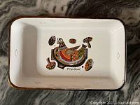 Front view of the rectangular metal dish showing full bird and abstract decorations and brown rim