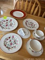 Eight stacked plates in varying sizes, two cups and saucers, serving pieces on wood table