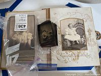 Showing antique photo album open with an ornate photo page and loose vintage photos in plastic bags