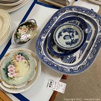 Photo showing the full assortment of nine pieces in varying blue and white and floral patterns stacked and displayed on a table.