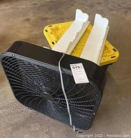 Black Holmes box fan placed in front of yellow plastic tote with lid and two white wall shelves.