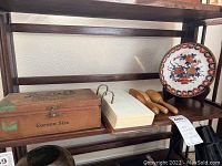 Photo of mid-shelf showing Rexall Drug wooden box, doctor's note pad and wooden sock darners alongside Chinese bowl on stand