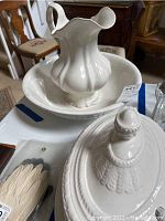 Photo of white ceramic pitcher inside matching shallow bowl on table