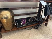 Side view showing the brass vase, cheese tray with tools, and black desk lamp on a wooden bench.