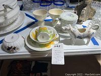 Overview of various fine china pieces including bowls, goblets, and cups arranged on table with a blue tape grid.