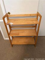 Front view of wooden folding bookshelf with three shelves assembled and standing upright.