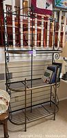 Full front view of metal French etagere or bakers rack showing three shelves, wrought iron scrollwork sides, and brass accents.