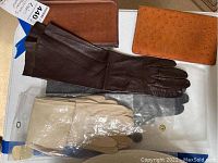 Overall display of two pairs of leather gloves and two leather wallets on white surface.