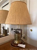 Side view of antique brass blow torch lamp showing pleated beige lampshade and wooden base