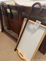Wooden folding luggage rack with black fabric straps, wooden cane leaning against it, and bed tray partially visible.