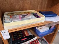 Two shelves containing various office supplies and scrapbooking materials including paper cutters, stencils, stickers, and decorative pipe cleaners.
