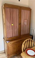Front view of vintage pine hutch cabinet with glass doors and red and white checkered curtains behind them. Wooden base with drawers and cupboard below.