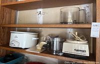 Photo of Rival Crock Pot, Cuisinart food processor base and attachments on wooden shelves.