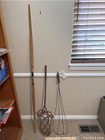 Full view of the three items: a tall wooden longbow, a woven wooden rug beater, and a wire rug beater with wooden handle