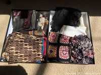 Top-down view of the entire scarf lot in a box showing multiple scarves folded in two sections.