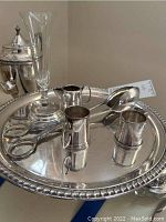 Silver plated cake stand with assorted silver plated tableware items on top, including a glass vase and serving pieces.