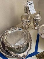 Silver plate coffee servers and three silver plate platters displayed showing the ornate designs and footed bases.