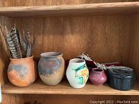 Five pottery items including Native carved stone box and pottery vases with various glaze colors and patterns arranged on wood shelf.