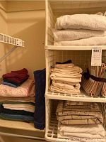 Folded assorted towels and linens stacked neatly on a shelf, showing different colors and patterns.
