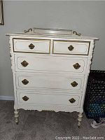Front view showing five drawers with brass handles and gold trim on white paint.